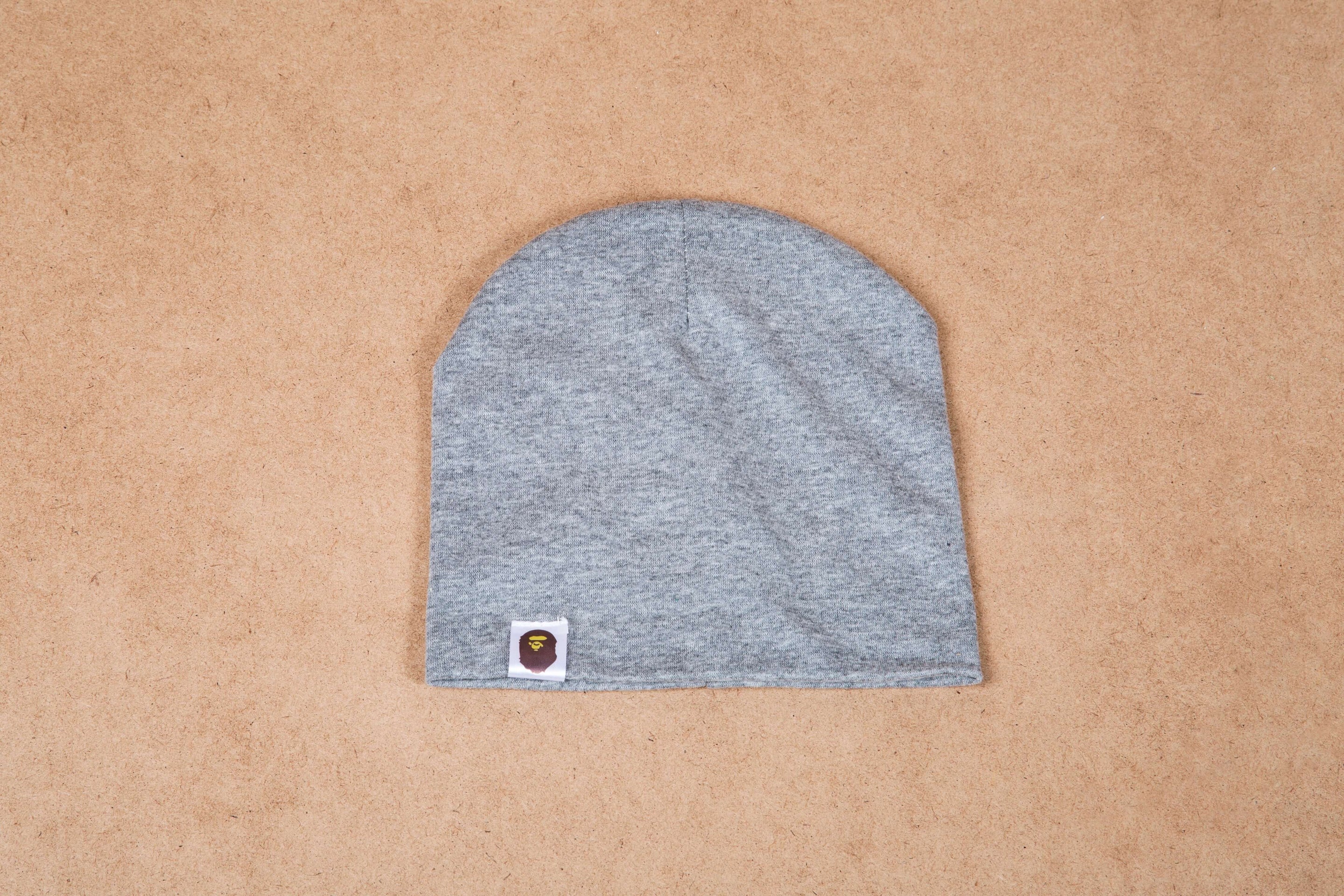 Gray beanie hat with small logo patch on beige background