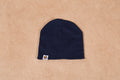 Navy blue beanie hat with small tag detail on beige background