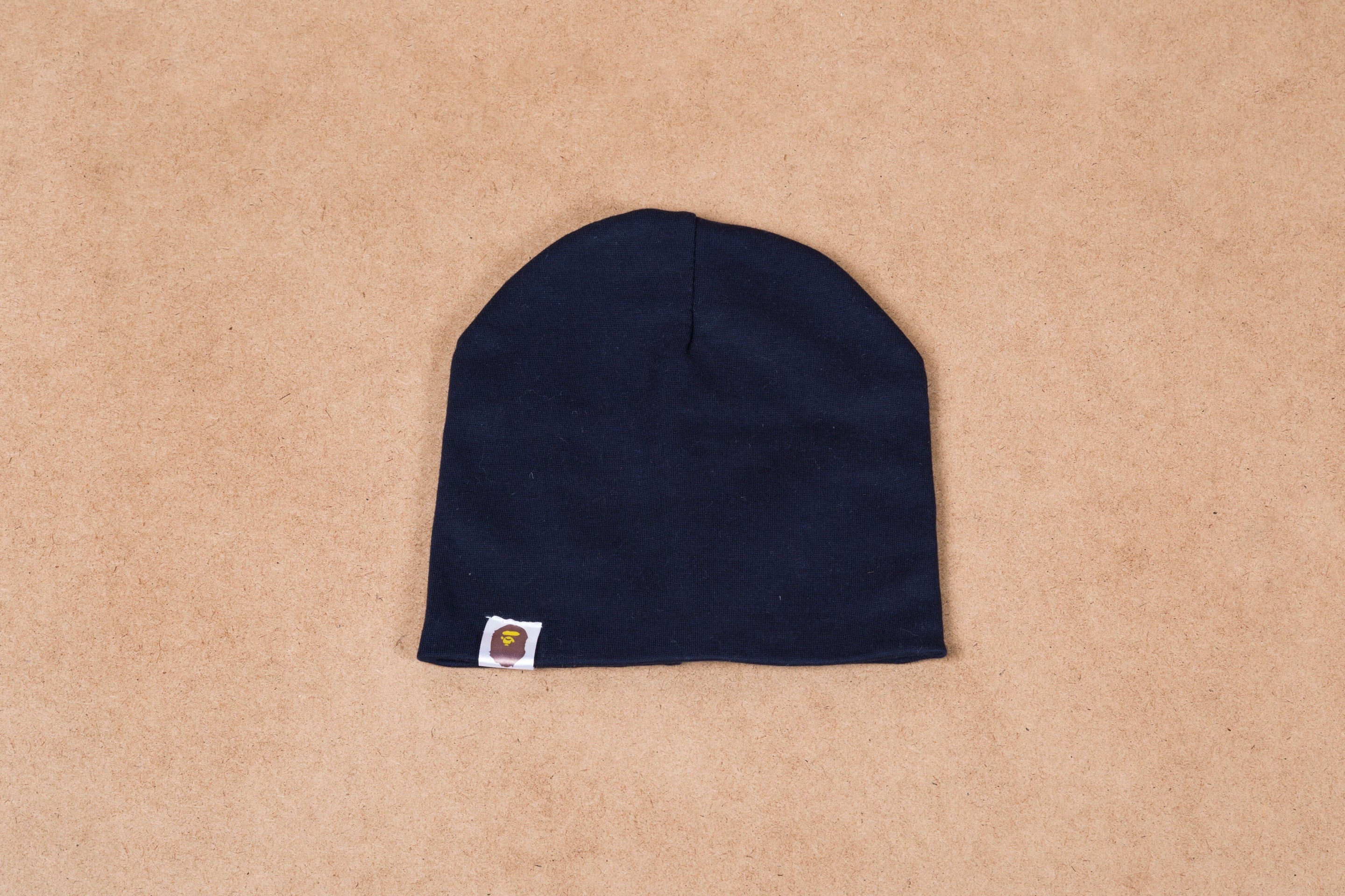 Navy blue beanie hat with small logo patch on tan background