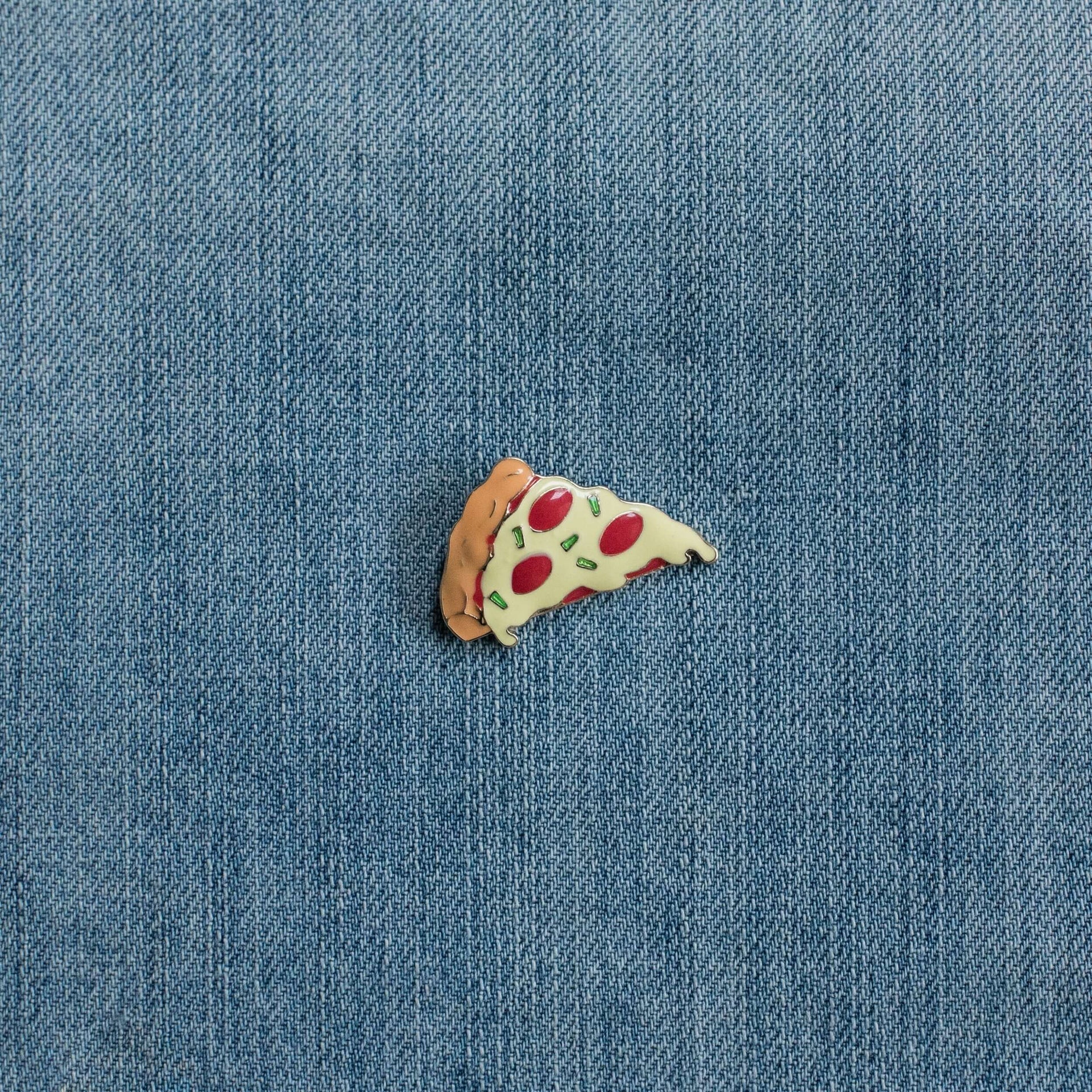 Pizza slice enamel pin on blue denim fabric background