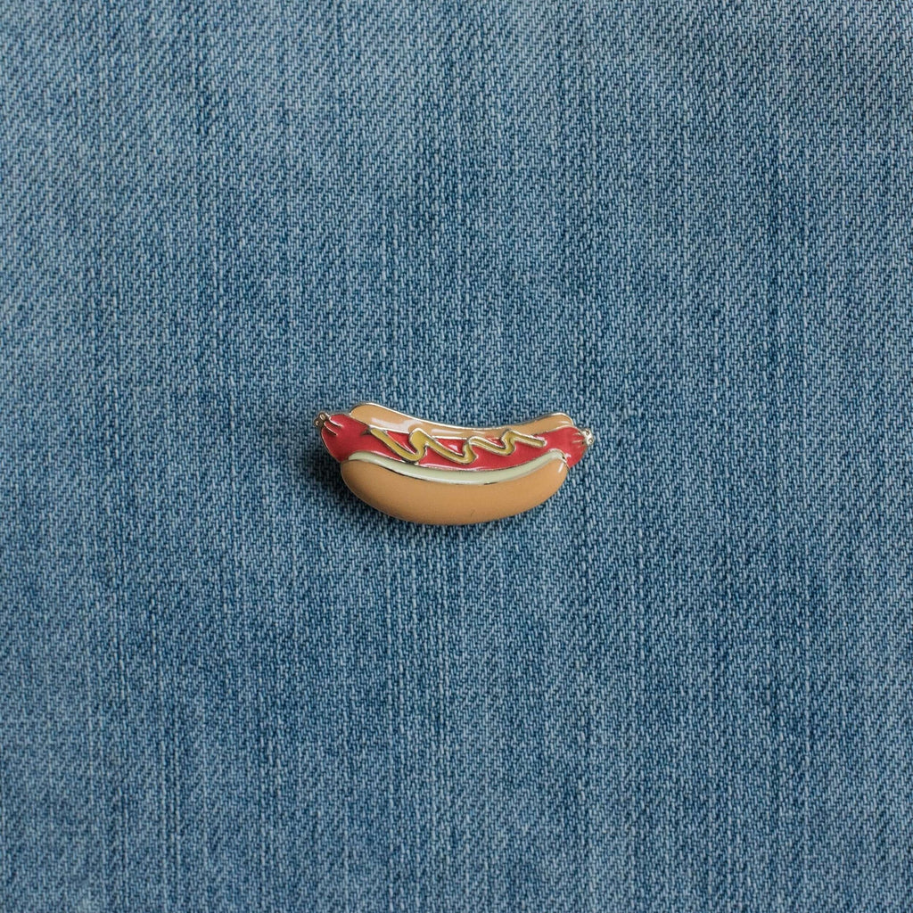 Hot dog enamel pin with ketchup and mustard on denim fabric background