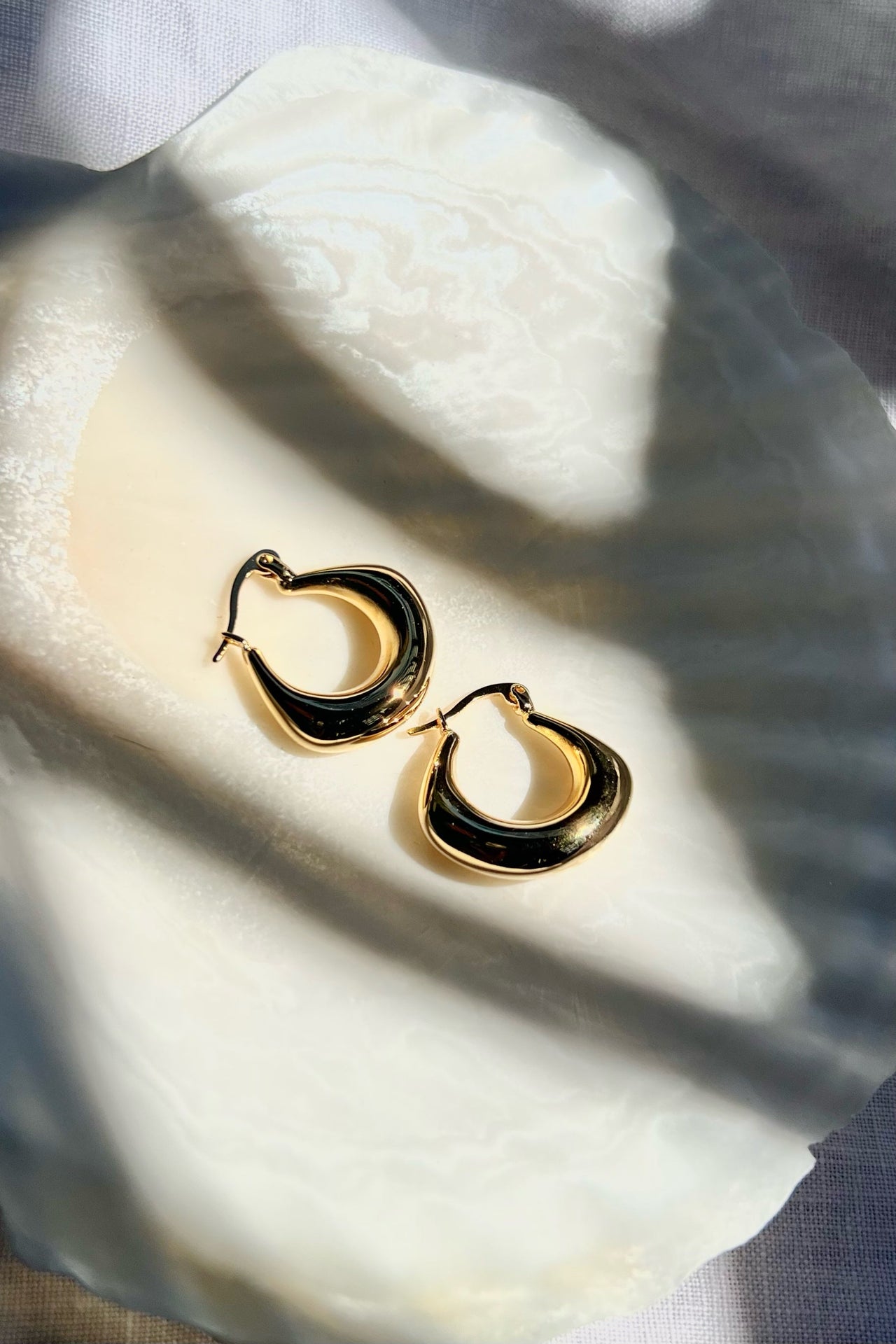 Pair of gold hoop earrings on a white shell dish in natural sunlight
