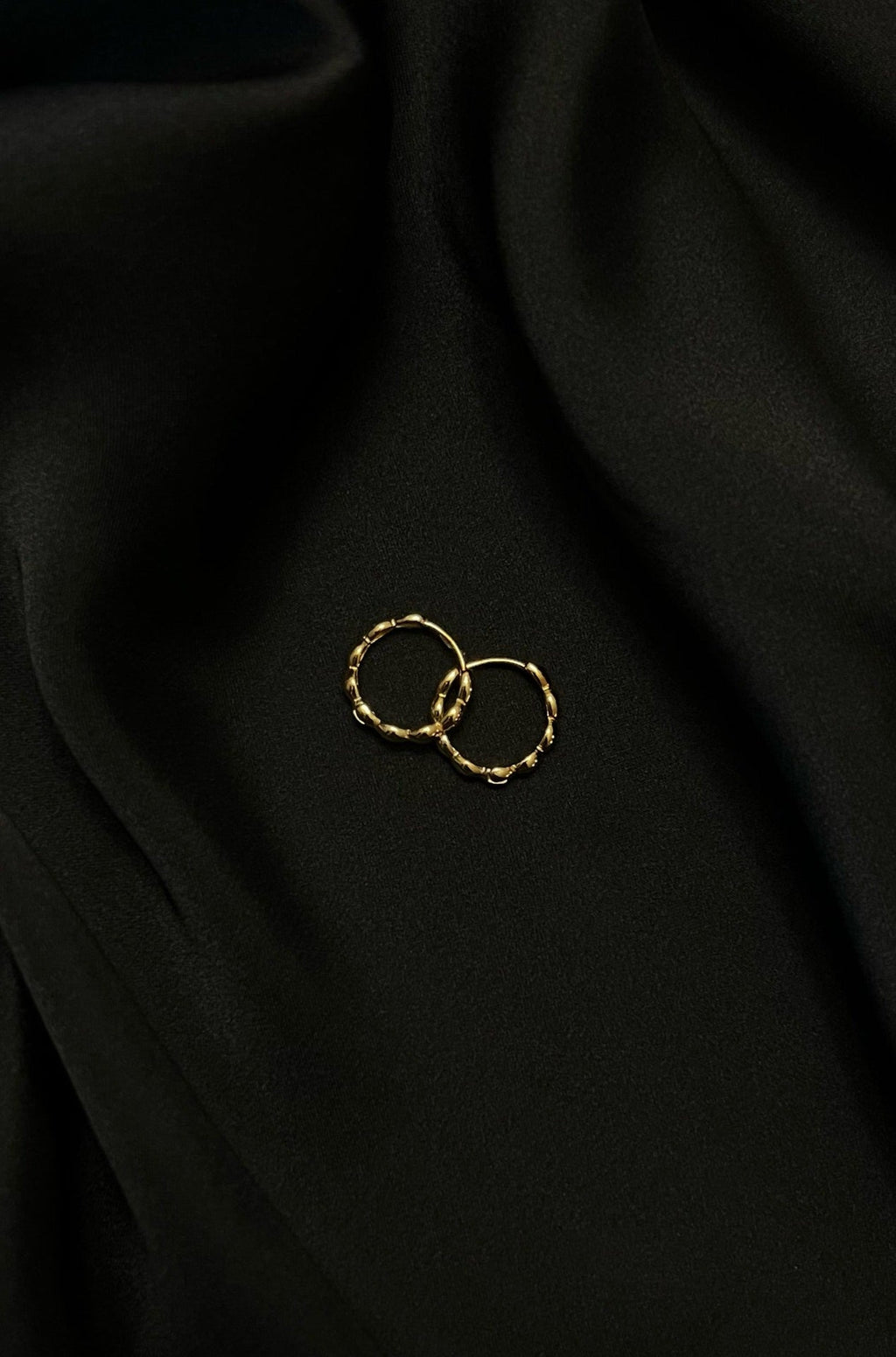 Gold hoop earrings with textured design on black silk fabric background