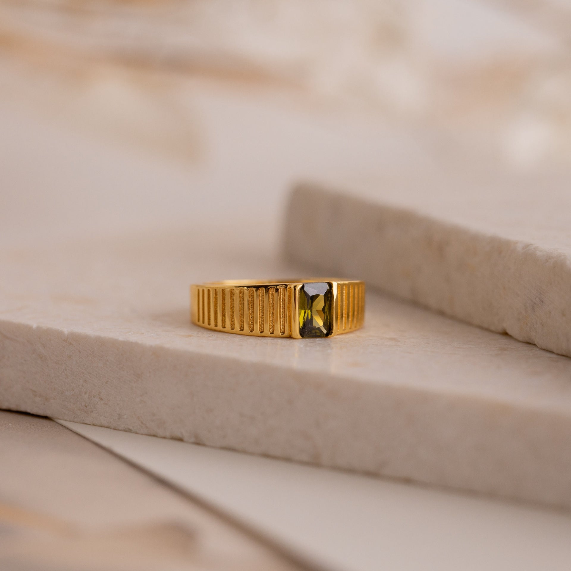 gold ring with rectangular green gemstone on stone slab, modern jewelry design