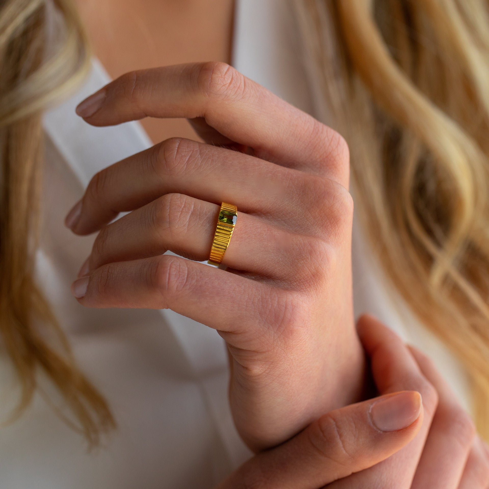 Gold textured ring with green gemstone worn on woman's hand
