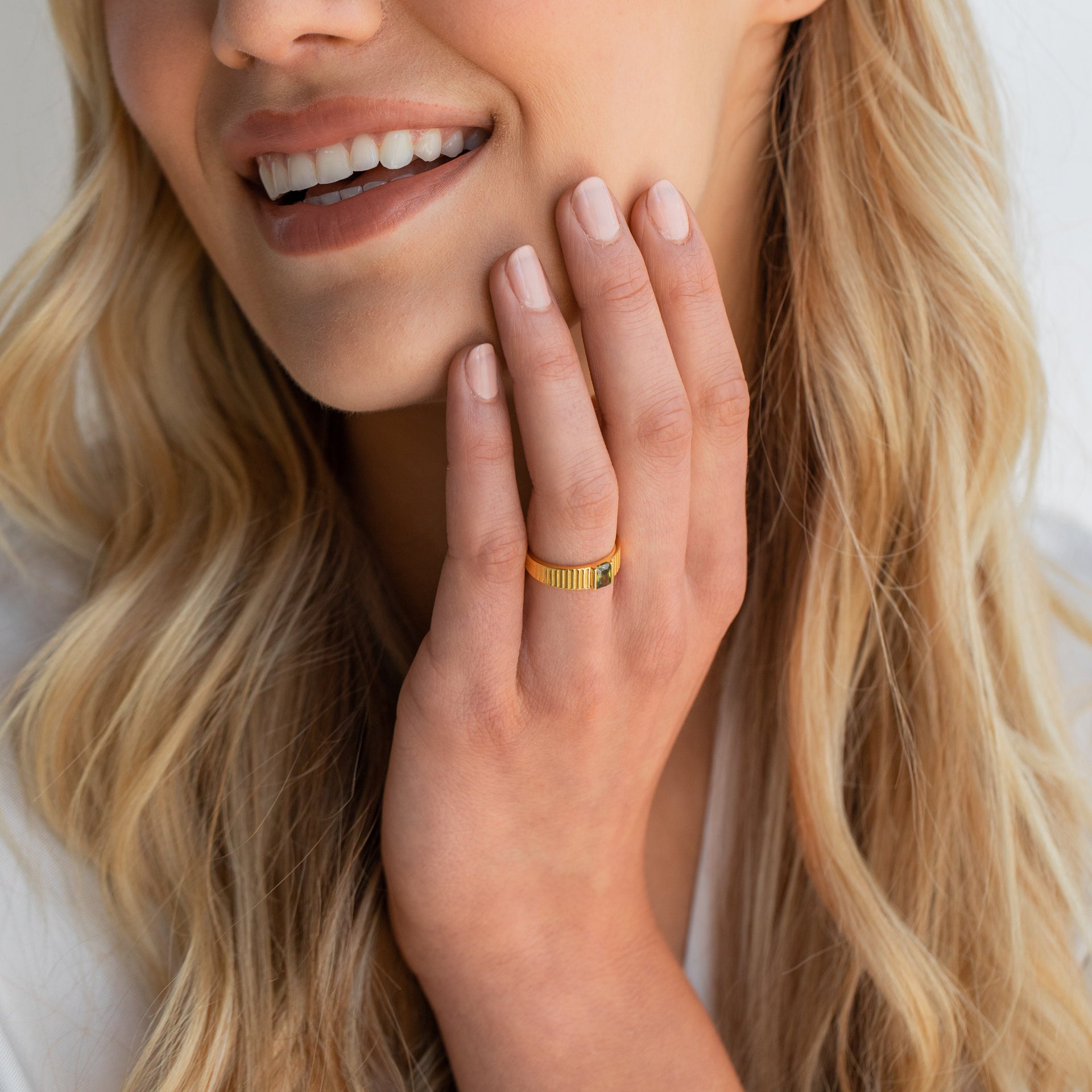 Smiling woman wearing gold band ring with gemstone, close-up jewelry detail