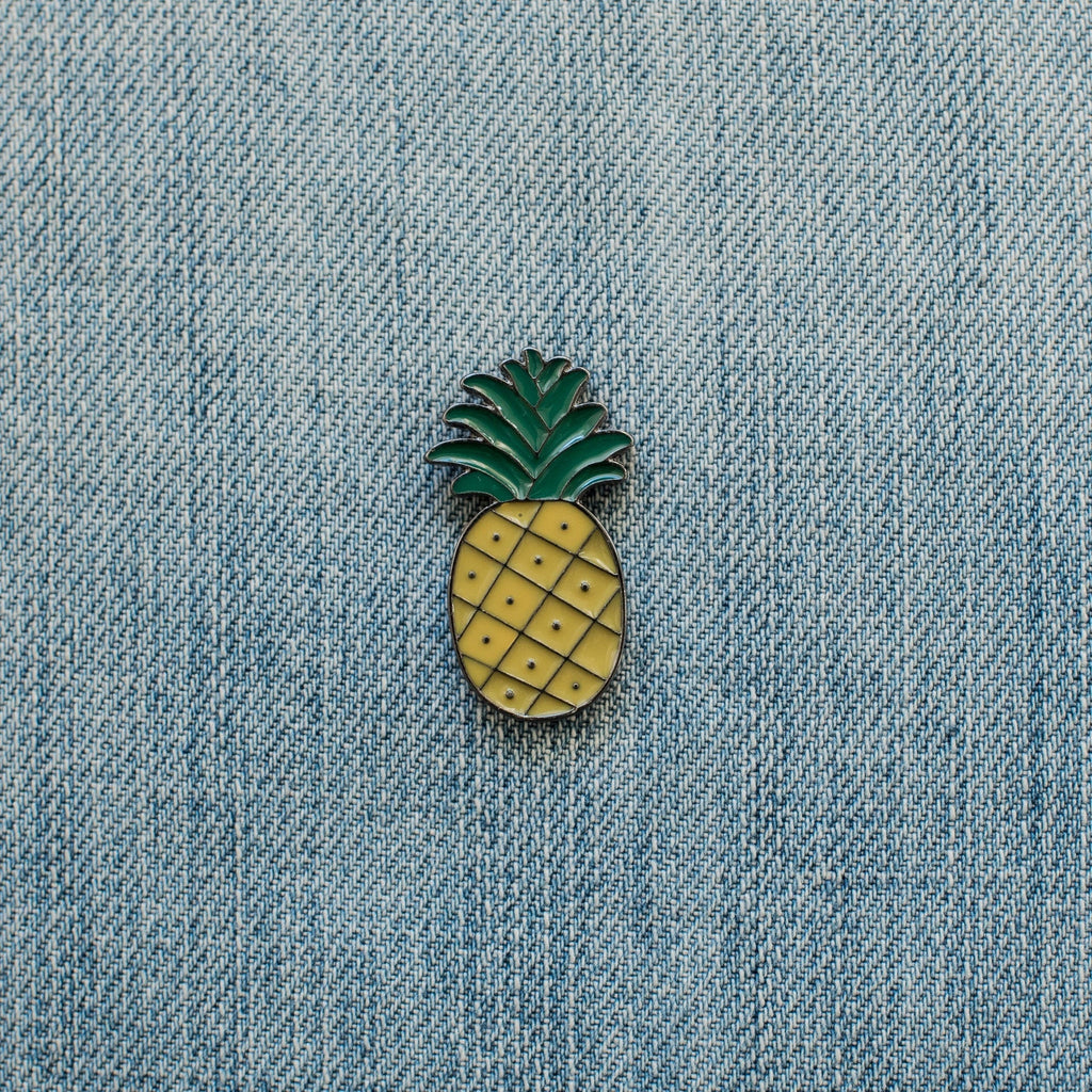 Pineapple enamel pin attached to light blue denim fabric.