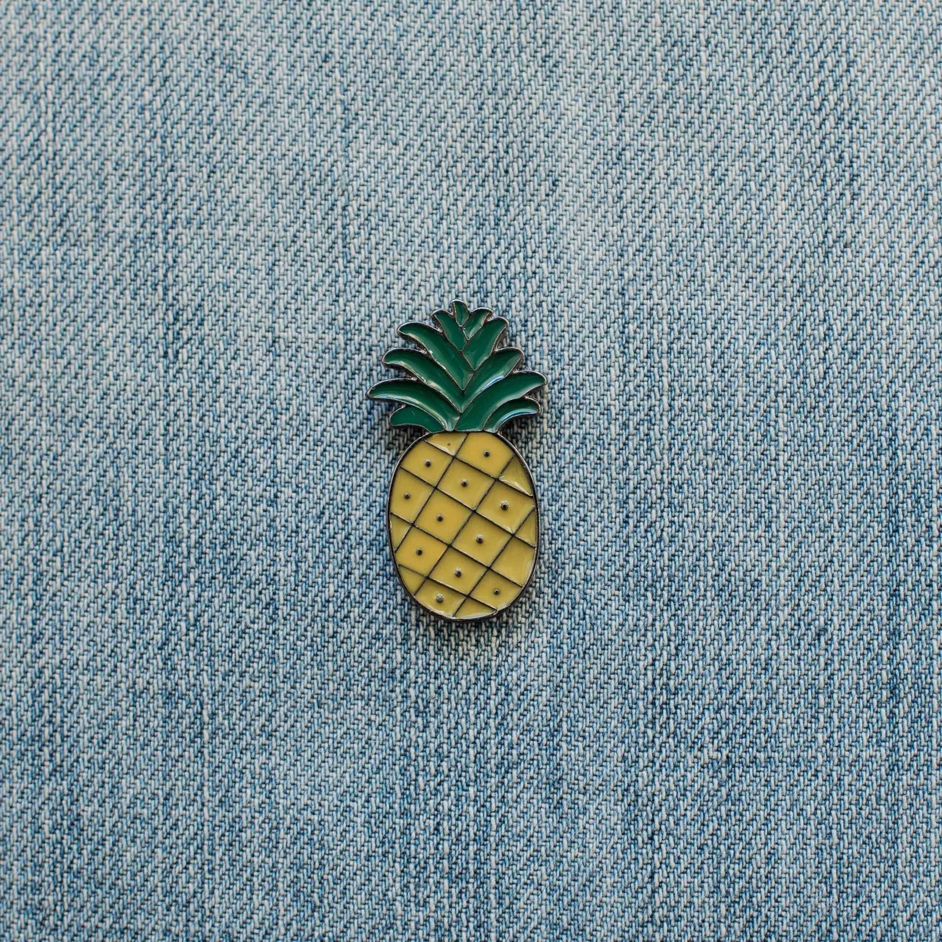 Pineapple enamel pin attached to light blue denim fabric.