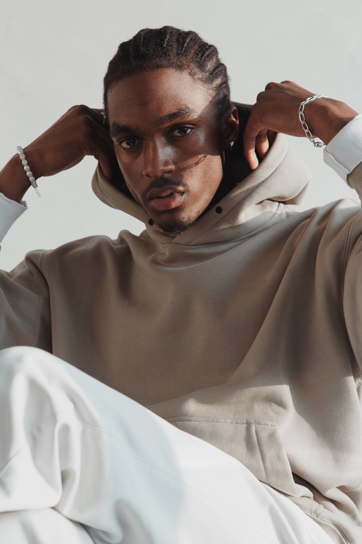 Man in beige hoodie and white pants posing against neutral background, fashion portrait