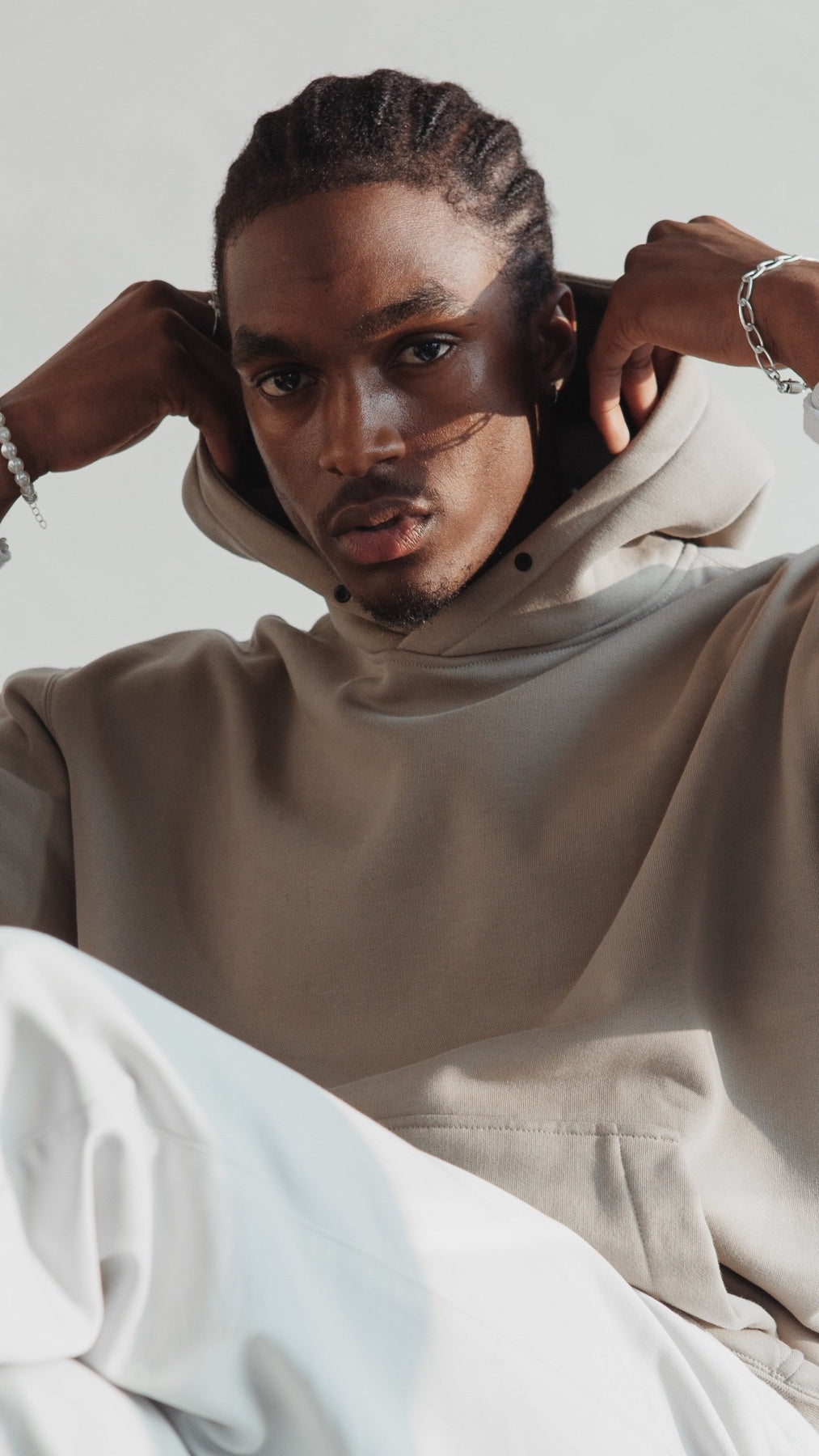 Man wearing beige hoodie and silver bracelet, seated in natural light