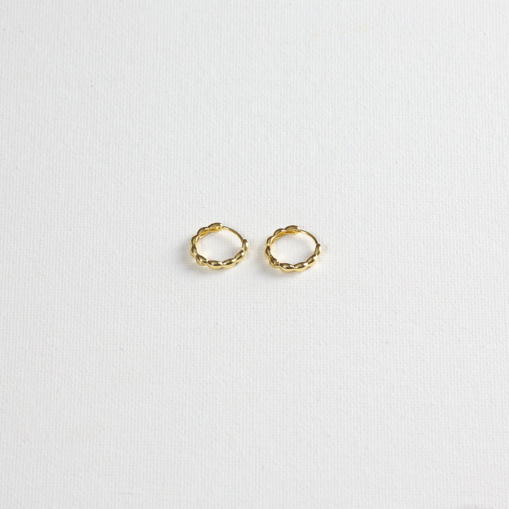 Pair of small gold twisted hoop earrings on a white textured background