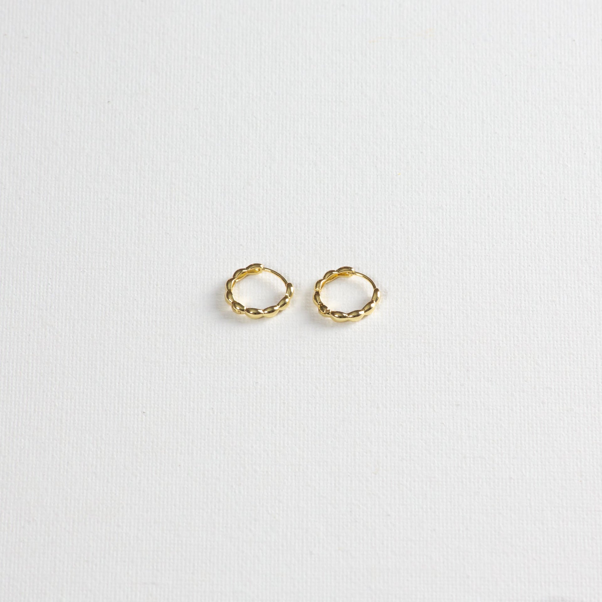 Pair of small gold twisted hoop earrings on a white textured background
