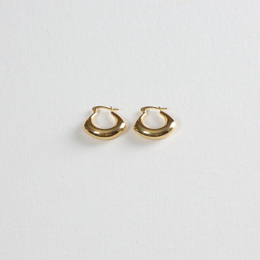 Pair of chunky gold hoop earrings on a white textured background