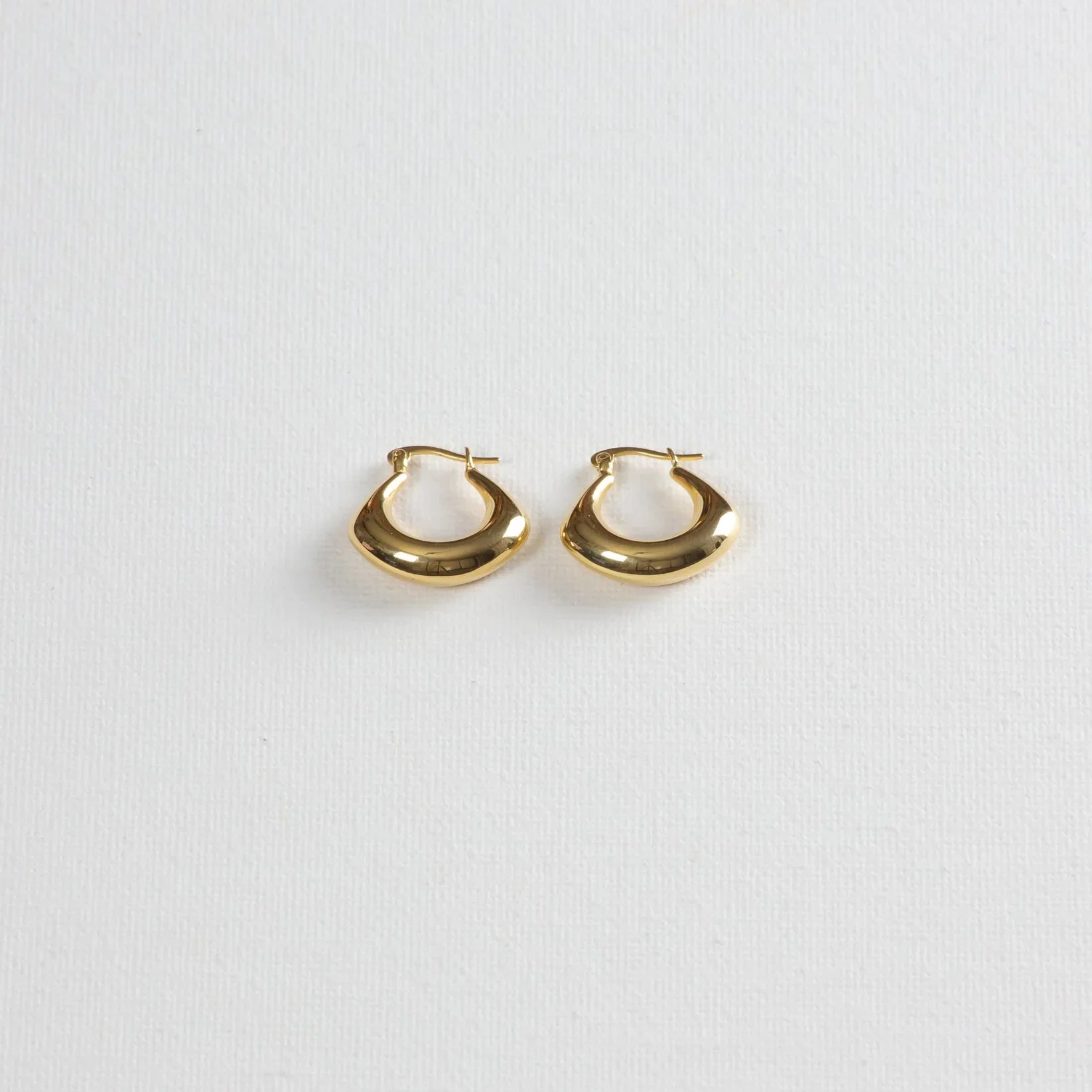 Pair of chunky gold hoop earrings on a white textured background