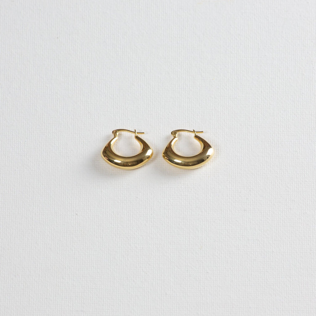 Gold chunky hoop earrings with smooth finish on white textured background